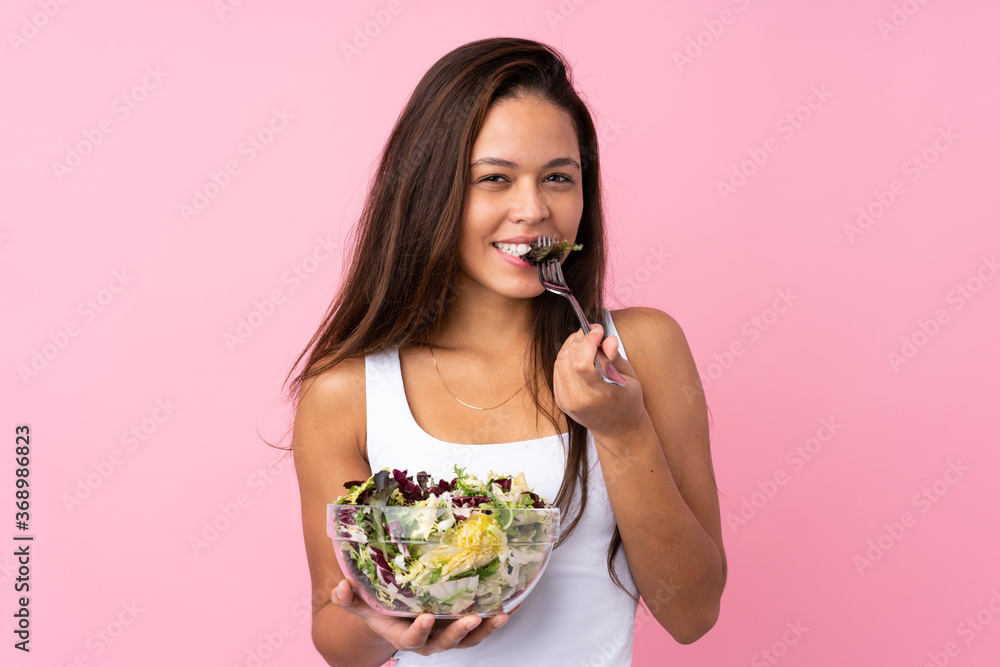 Young Brazilian girl with healthy salad over isolated pink background