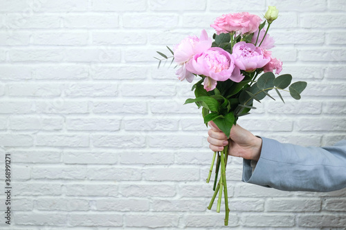 Flower delivery concept of packing flowers. The girl holds pink peonies, against the background of a white brick wall