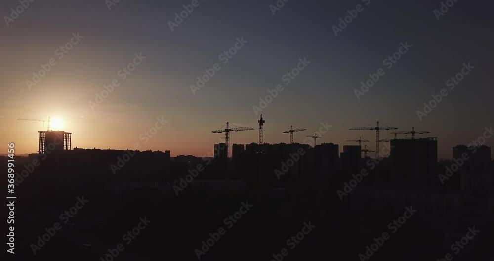 Takeoff of the drone against the backdrop of the sunset and the silhouette of houses under construction and construction cranes and equipment Takeoff of the drone against the backdrop of the sunset and the silhouette of houses under construction and construction cranes and equipment