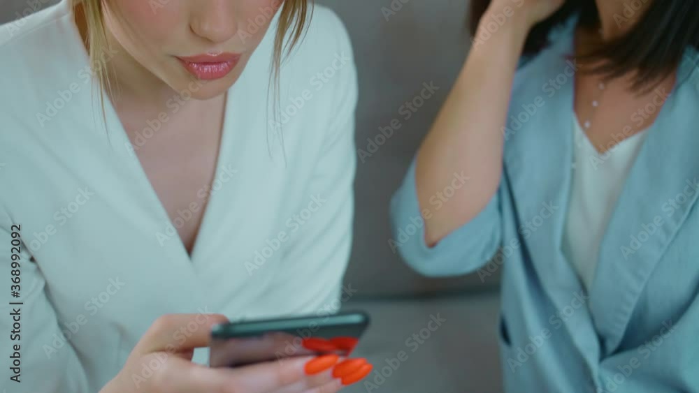 Happy women chat and look at the phone, Girls smile and show each other photos, Friends sit on the couch at home and talk Happy women chat and look at the phone, Girls smile and show each other photos, Friends sit on the couch at home and talk