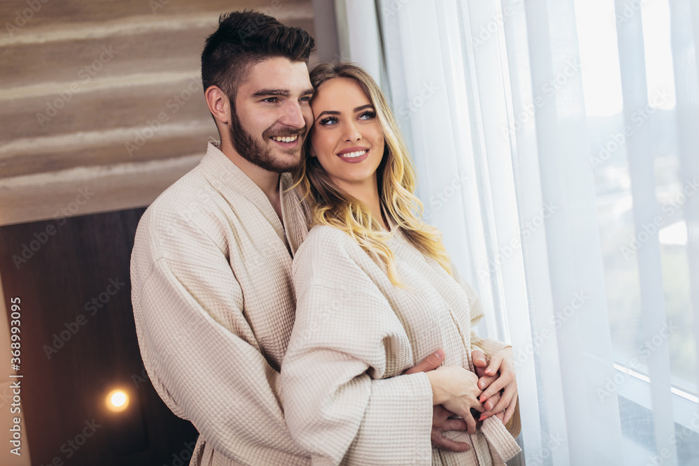 Young happy couple in hotel room in the morning. Just married man and woman standing at window.