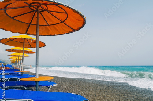 Perfect summer vacation destination. Straw umbrellas and sunbeds on the empty pebble beach with sea in the background. Vacation and tourism concept. Sunbeds on the paradise Beach
