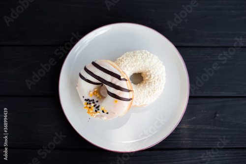 Top-view of two assorted donuts on a small white plate with black background. Fresh sweet colorful homemade vanilla donuts on vintage background for birthday or party, free space for text