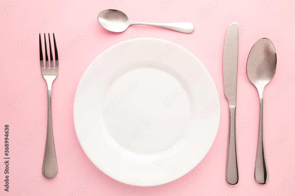 Table setting with white plates, and cutlery - fork, spoon and knife. Shot from above. Copy space on empty plate.