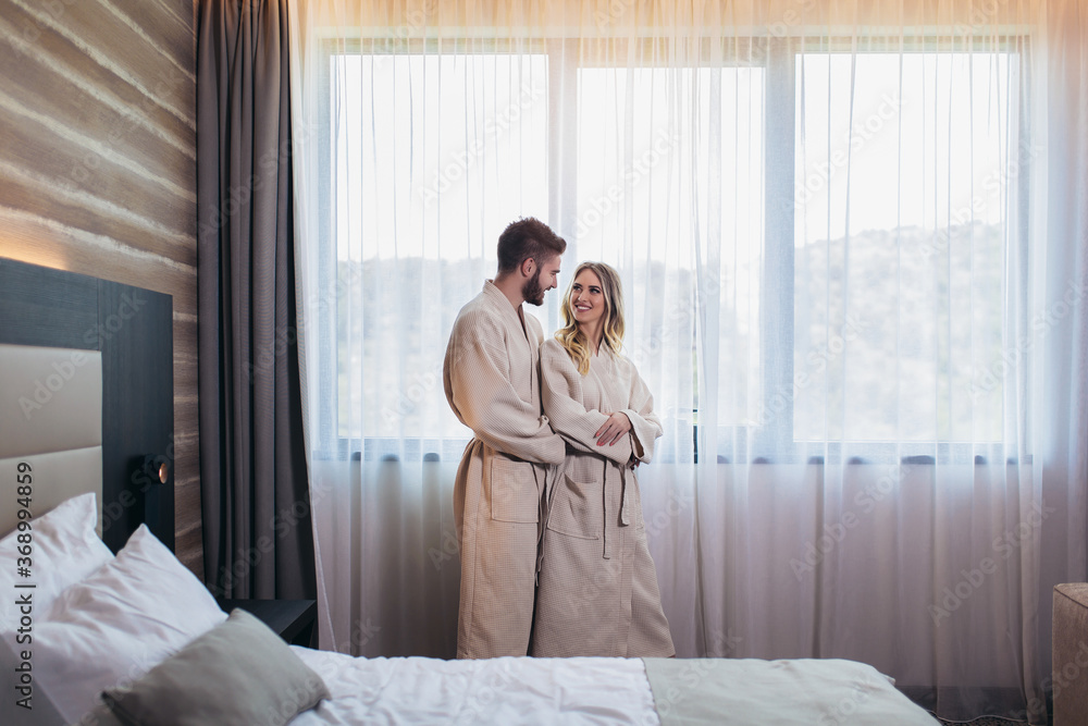 Young happy couple in hotel room in the morning. Just married man and woman standing at window. Young happy couple in hotel room in the morning. Just married man and woman standing at window.