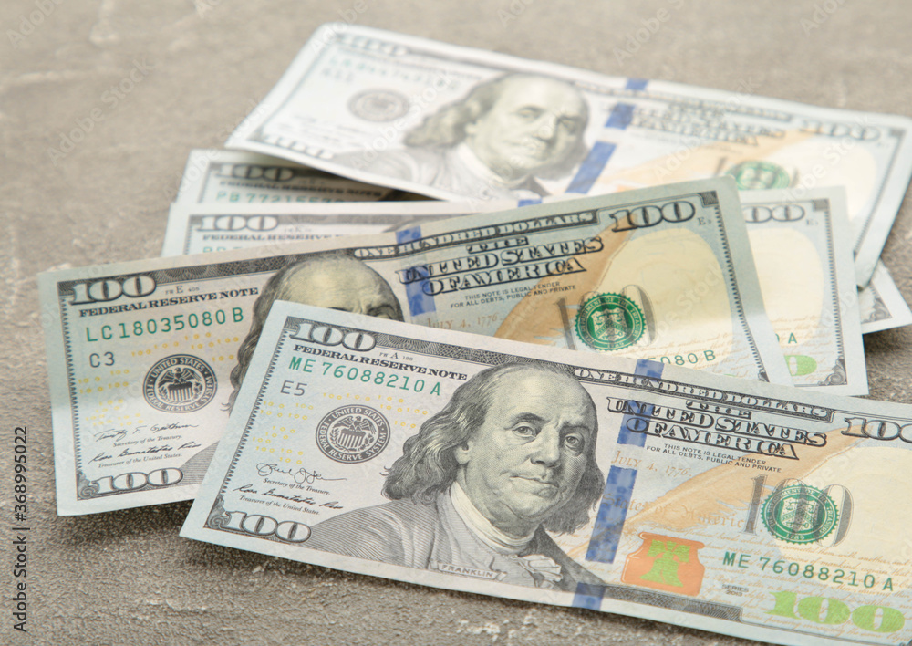 A pile of hundred dollar bills on grey background with copy space A pile of hundred dollar bills on grey background with copy space