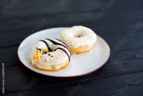 Close-up of two assorted donuts on a small white plate with black background. Fresh sweet colorful homemade vanilla donuts on vintage background for birthday or party, free space for text