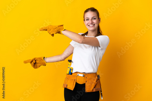 Young electrician woman isolated on yellow background pointing finger to the side and presenting a product photo