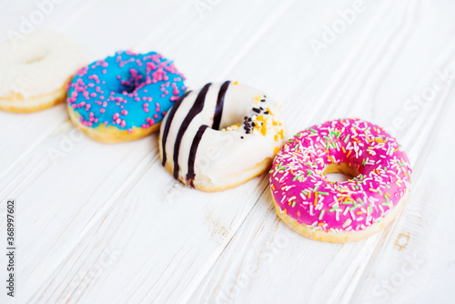 Row of four tasty colorful donuts on a white wooden vintage background. Sweet and colorful donuts. Dessert. Homemade sweets. Café dessert for birthday or party, top view, with copy space