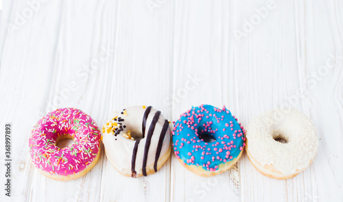 Row of four tasty colorful donuts on a white wooden background. Sweet and colorful donuts. Dessert. Homemade sweets. Café dessert for birthday or party, top view, with copy space