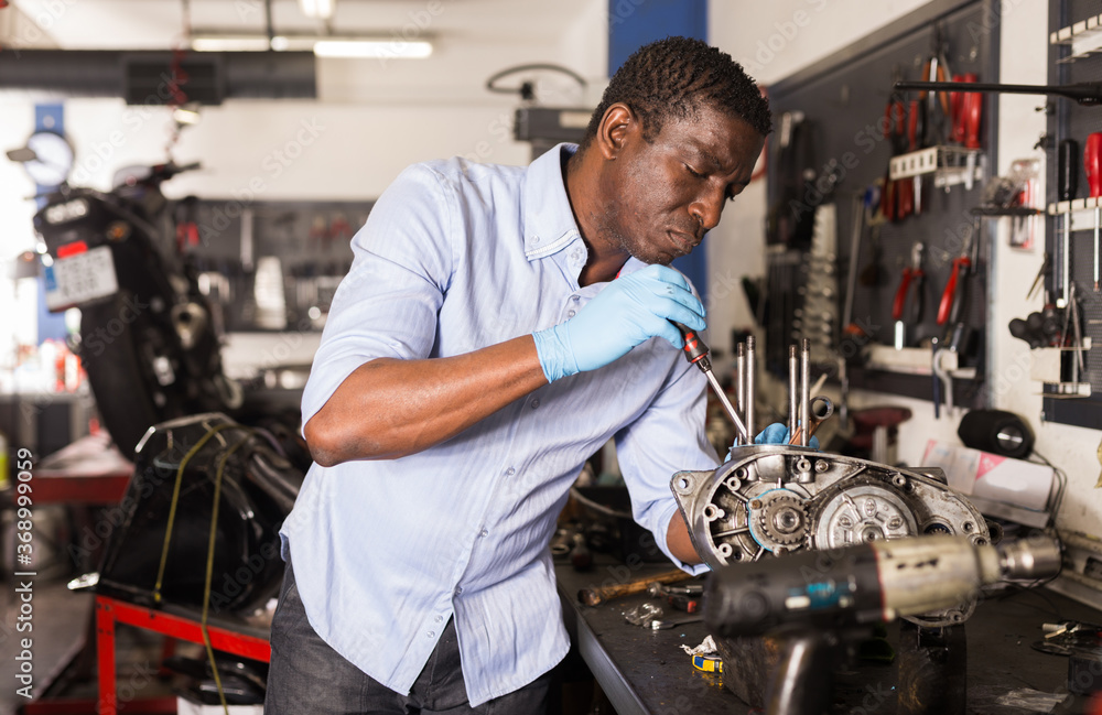 Afro american worker repairing a motorcycle engine in a garage. High quality photo