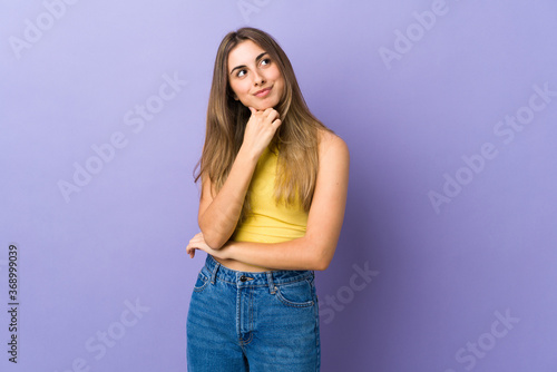 Young woman over isolated purple background and looking up © luismolinero