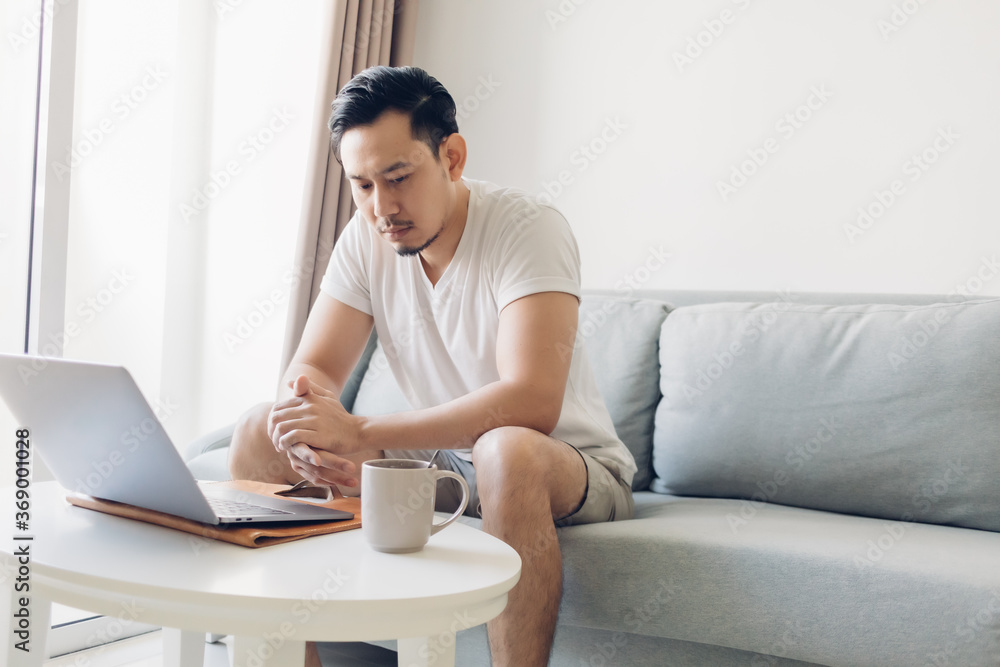 Serious Asian man is working on his laptop in the living room. Serious Asian man is working on his laptop in the living room.