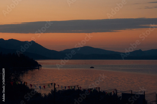 the boat sails to the shore of the lake, covered with trees in the mountains at sunset