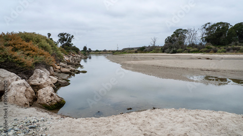 Rocks and shrubs divide the slough from the Pacific Ocean in this shallow waterway along Goleta Beach Park, Santa Barbara, California