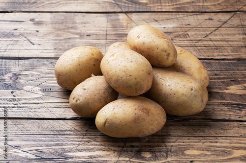 Several tubers of raw potatoes on a wooden background. Copy space.