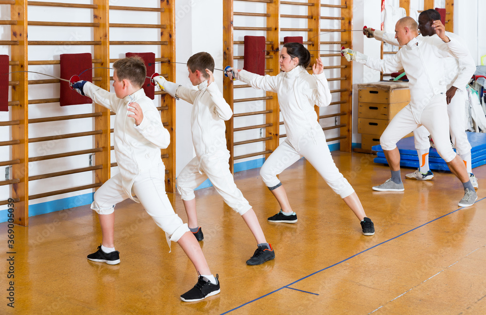 Mixed age group of athletes at fencing workout, training attack movements on mannequins