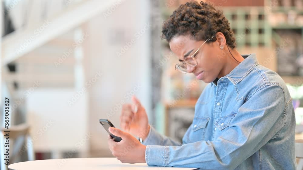 Upset African Woman reacting to Loss on Smartphone at Cafe Upset African Woman reacting to Loss on Smartphone at Cafe