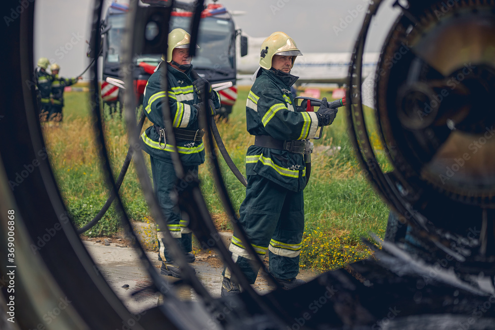 Portrait of two firemen in fireproof uniform splashing water from water hose Portrait of two firemen in fireproof uniform splashing water from water hose