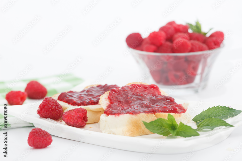 Raspberry jam with fresh raspberries and bread slices on white plate. Homemade marmalade, perfect for light, sweet breakfast.