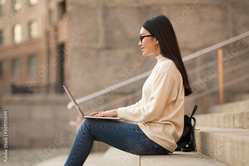 Student in specs using laptop, sitting on stairs