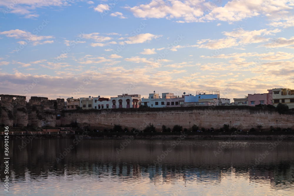 View of the embankment, Bassin Souani, colorful houses, ruins of ancient stables and reflection in the water, Meknes city, Morocco