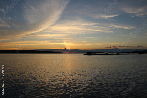 The sun setting into the clouds, blue sky with Cirrus clouds and the lake Vesijärvi. Lahti. Finland. © Elena