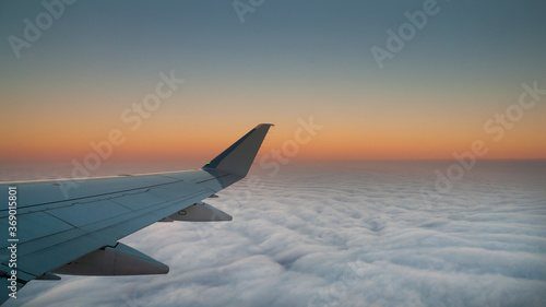 Looking out the window of the airplane at dawn or dusk with clouds below, colorful peaceful image of flight, transportation, vacation, travel