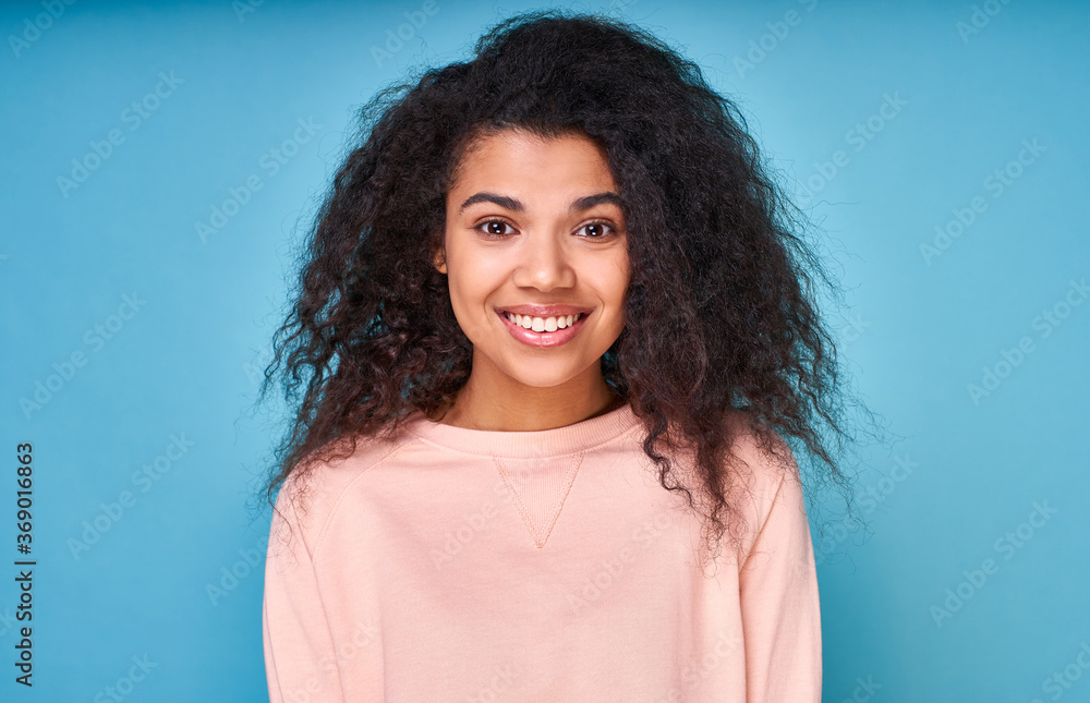 Fototapeta premium Portrait of an attractive smiling curly dark-skinned lady on a blue background.