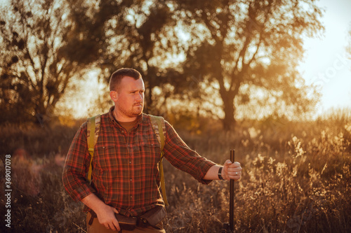 Irish looking red bearded hunter in checkered shirt staying outdoors in the sunset light and holding his gun © honey_inside