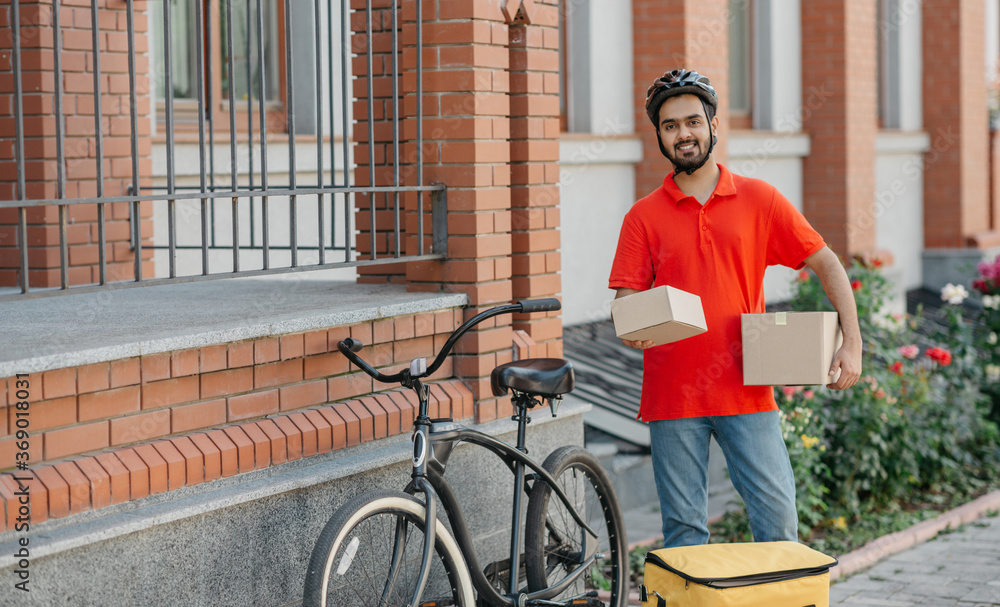 Obraz premium Fast delivery for many online purchases. Smiling courier with beard holds cardboard boxes