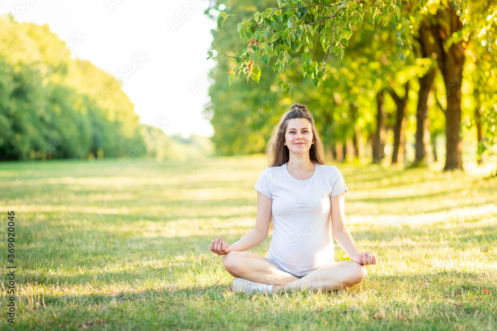 a pregnant girl does sports in nature in the summer, yoga for pregnant women in the fresh air