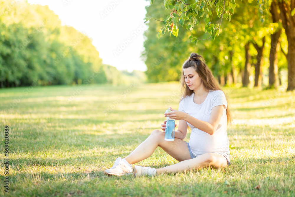 a pregnant girl does sports in nature in the summer and drinks water from a bottle, yoga for pregnant women in the fresh air a pregnant girl does sports in nature in the summer and drinks water from a bottle, yoga for pregnant women in the fresh air
