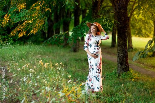 a pregnant woman in a dress and hat walks in the forest in summer  a pregnant girl s walk in nature