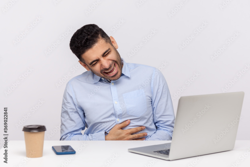 Amused businessman sitting office workplace with laptop on desk, holding his belly and laughing out loud, feeling carefree, being hysterical at funny joke. studio shot isolated on white background Amused businessman sitting office workplace with laptop on desk, holding his belly and laughing out loud, feeling carefree, being hysterical at funny joke. studio shot isolated on white background