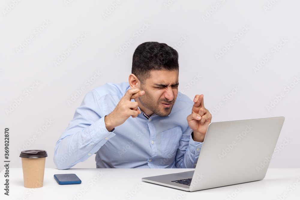 Man employee sitting office workplace keeping eyes closed and fingers crossed for good luck, wishing fortune, dreaming of promotion, successful business plan. studio shot isolated on white background Man employee sitting office workplace keeping eyes closed and fingers crossed for good luck, wishing fortune, dreaming of promotion, successful business plan. studio shot isolated on white background