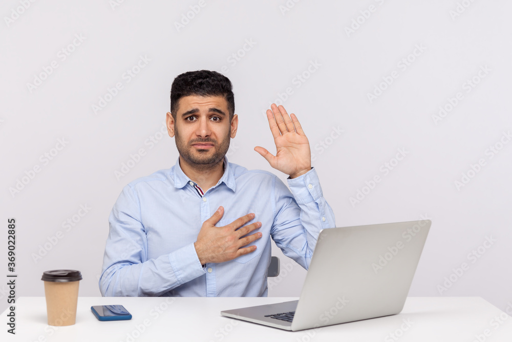 I swear! Honest businessman sitting office workplace with laptop on desk, raising hand, touching chest and making sincere promise, looking trustworthy reliable. studio shot isolated, white background I swear! Honest businessman sitting office workplace with laptop on desk, raising hand, touching chest and making sincere promise, looking trustworthy reliable. studio shot isolated, white background