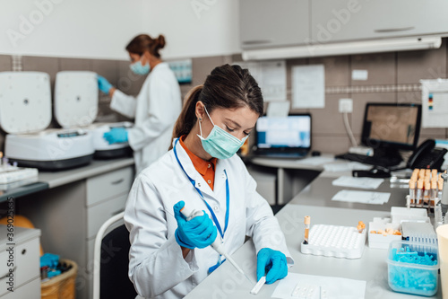 Two female scientists or technicians with face protective masks work in laboratory on human blood samples.