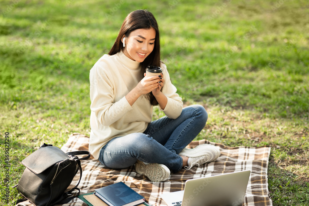Student drinking coffee, using laptop, sitting in the park Student drinking coffee, using laptop, sitting in the park