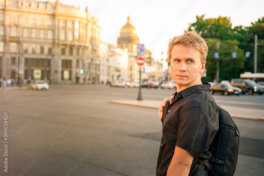A young blond man walks along the Palace square in the summer evening with a view of St. Isaac's Cathedral in St. Petersburg