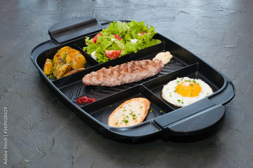 Breakfast, cutlet or steak, tomato salad, fried potatoes, croutons and fried egg on black plate. Restaurant lunch, content for the site Breakfast, cutlet or steak, tomato salad, fried potatoes, croutons and fried egg on black plate. Restaurant lunch, content for the site
