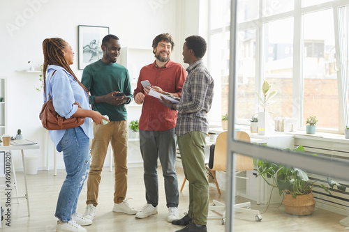 Full length portrait of multi-ethnic group of people dressed in casual wear and smiling cheerfully while discussing work standing in office photo