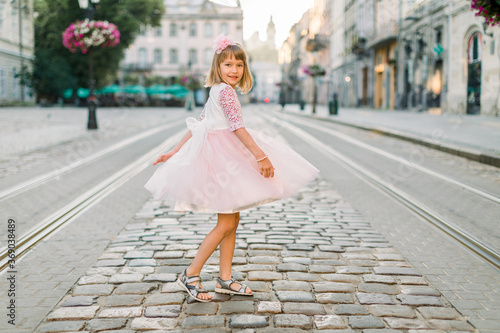 Little girl in pink dress and flower in her hair walking through the streets of the old town in Lviv, Ukraine