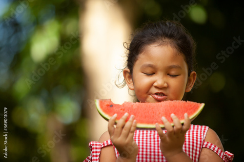 cute little girl eating watermelon on the grass in summertime with happiness