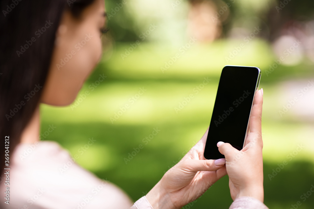 Woman using smartphone with blank black screen outdoors, mockup