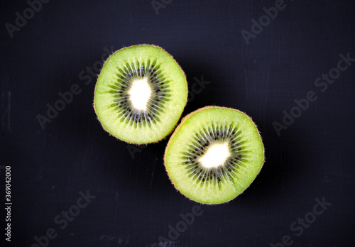 Cut, sliced fresh Kiwi fruit isolated, overlay on acrylic black scratchy grunge painting on canvas background. Overhead, top view shot. Still life, food photography related concepts.