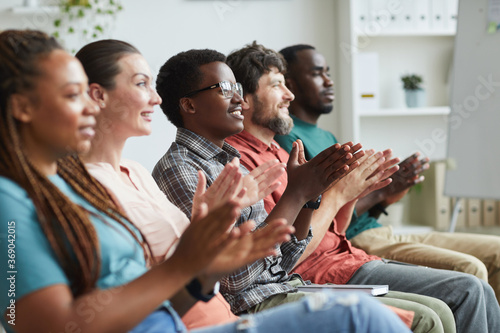 Side view portrait of multi-ethnic group of people applauding while sitting in row in audience or conference room, copy space