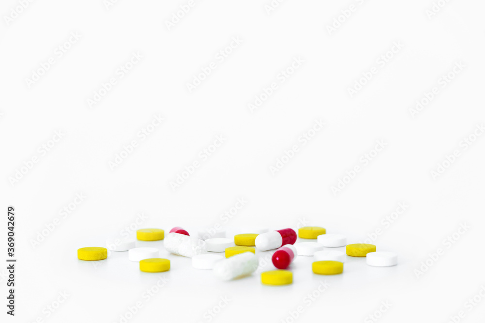 Multicolored medicines pills scattered on white table. White, yellow and red capsules. Pharmaceutical drug isolated copy space minimalistic background Multicolored medicines pills scattered on white table. White, yellow and red capsules. Pharmaceutical drug isolated copy space minimalistic background