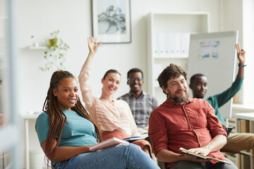 Multi-ethnic group of people raising hands while answering questions during training seminar or business conference in office, copy space