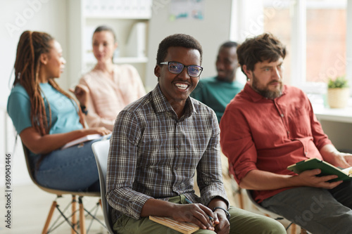 Multi-ethnic group of people sitting in audience during training seminar or business conference in office, focus on young African-American man smiling at camera in foreground, copy space